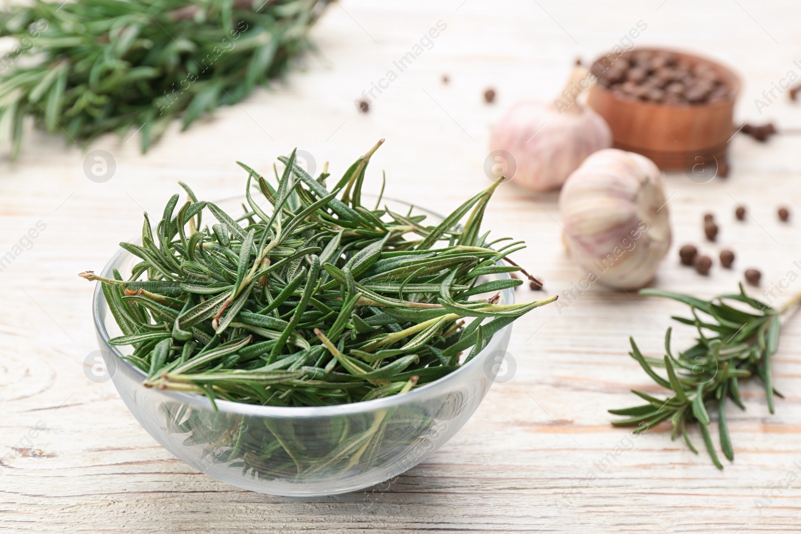 Photo of Fresh rosemary in glass bowl on white wooden table