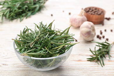 Photo of Fresh rosemary in glass bowl on white wooden table