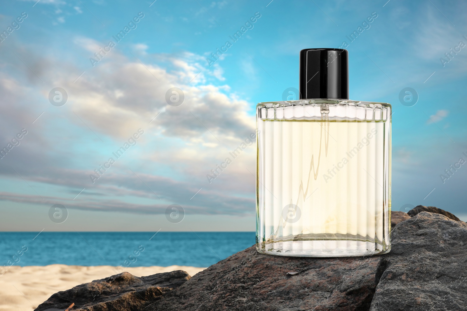 Image of Bottle of aquatic perfume on rock near ocean. Fresh sea breeze scent