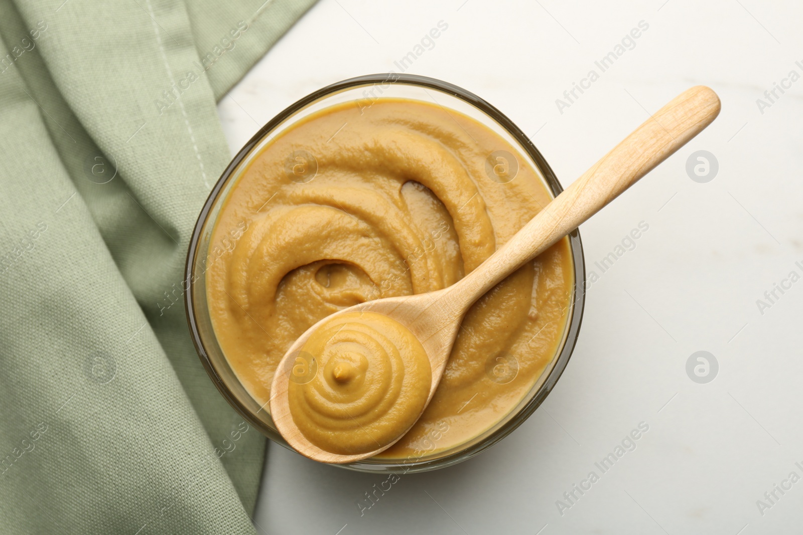 Photo of Bowl and spoon with tasty mustard sauce on white table, top view