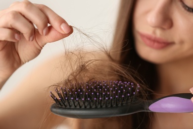 Woman untangling her hair from brush on light background, closeup