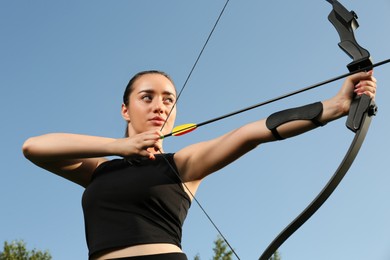 Photo of Woman with bow and arrow practicing archery outdoors, low angle view