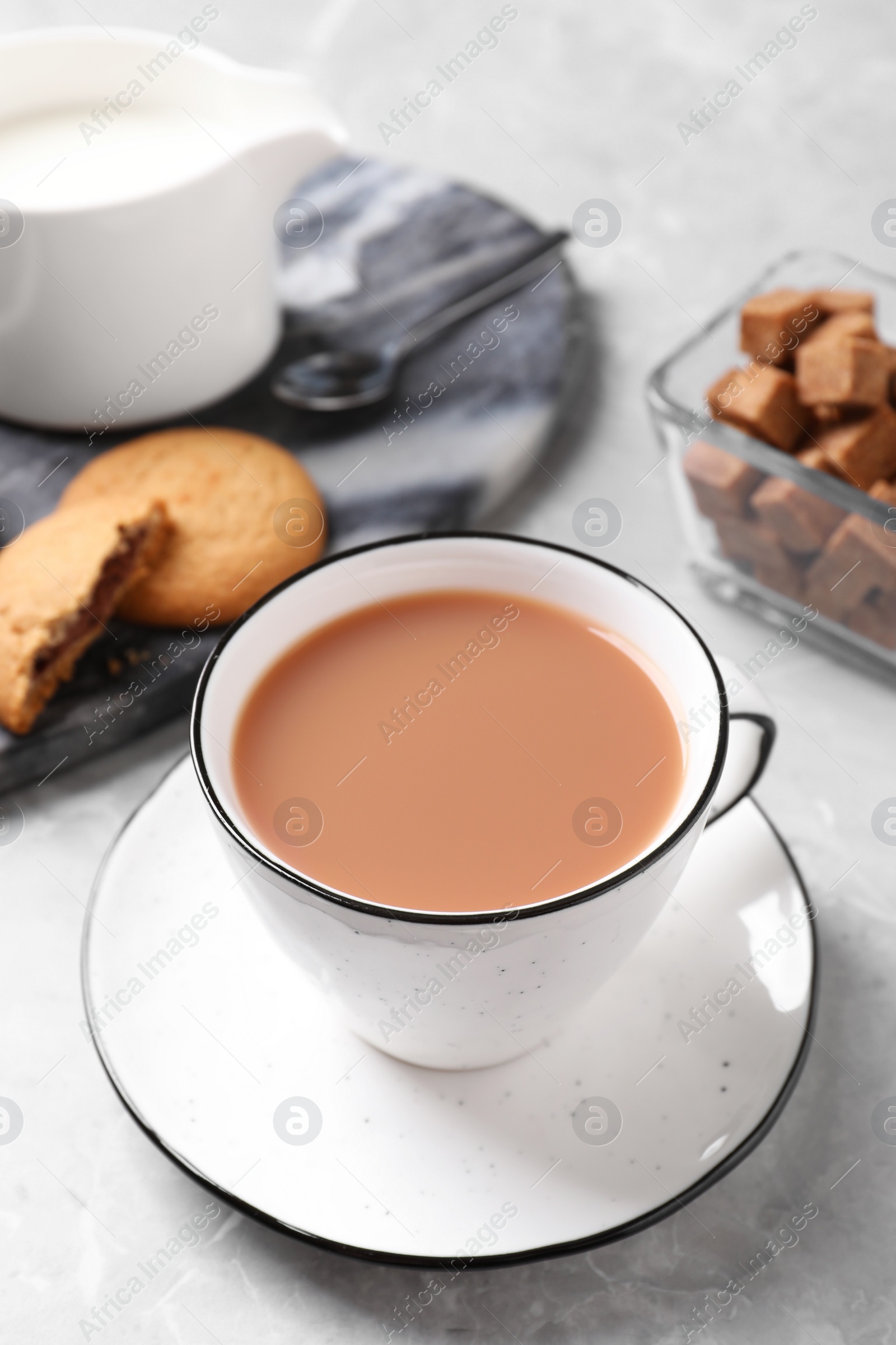 Photo of Delicious tea with milk in white cup near cookies on grey table