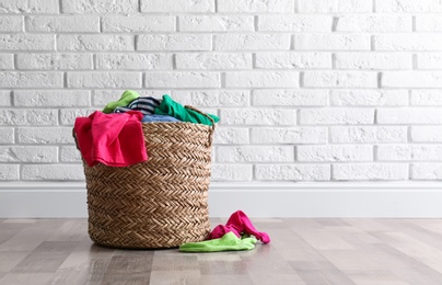 Photo of Wicker basket with dirty laundry on floor near white brick wall
