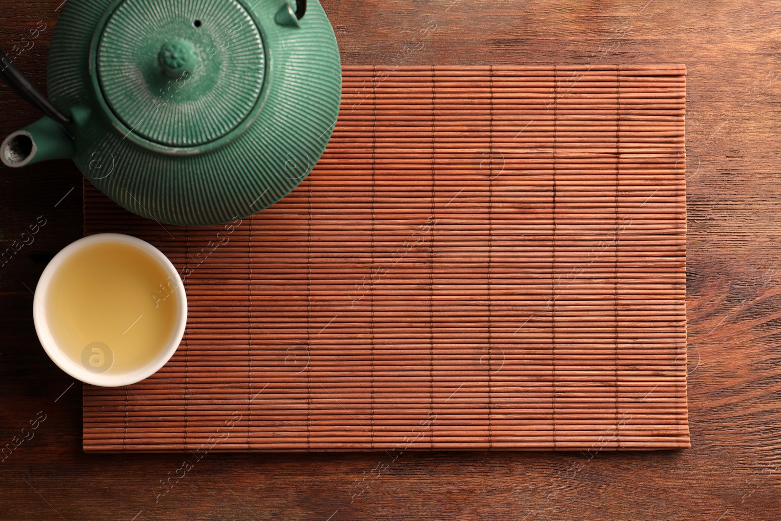 Photo of Bamboo mat, teapot and cup of tea on wooden table, top view. Space for text