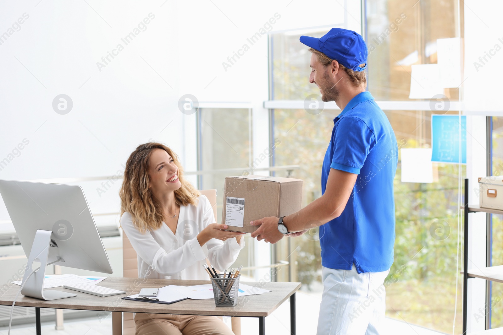 Photo of Young woman receiving parcel from courier in office