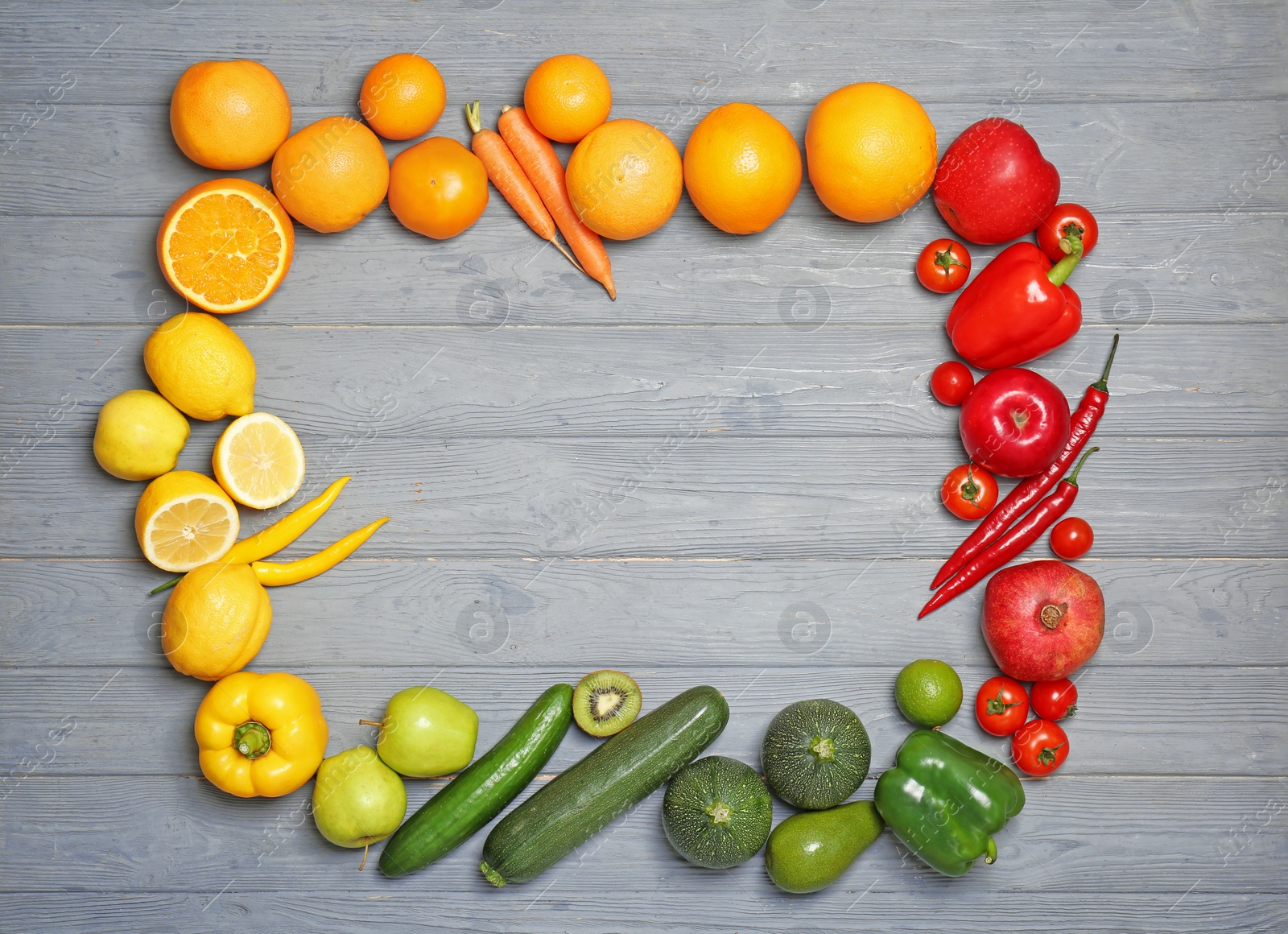 Photo of Frame made of ripe fruits and vegetables in rainbow colors on grey background, top view