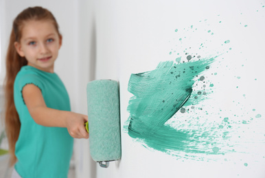 Little girl painting white wall indoors, focus on hand