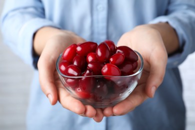 Photo of Woman with glass bowl of fresh ripe dogwood berries on light background, closeup
