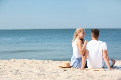 Happy young couple sitting together at beach on sunny day