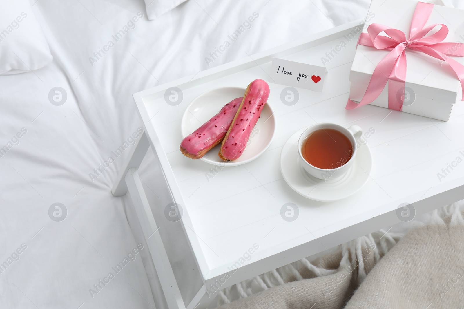 Photo of Tasty breakfast served in bed. Delicious eclairs, tea, gift box and I Love You card on tray, above view