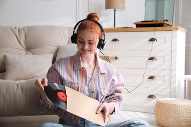 Photo of Young woman listening to music with turntable in living room