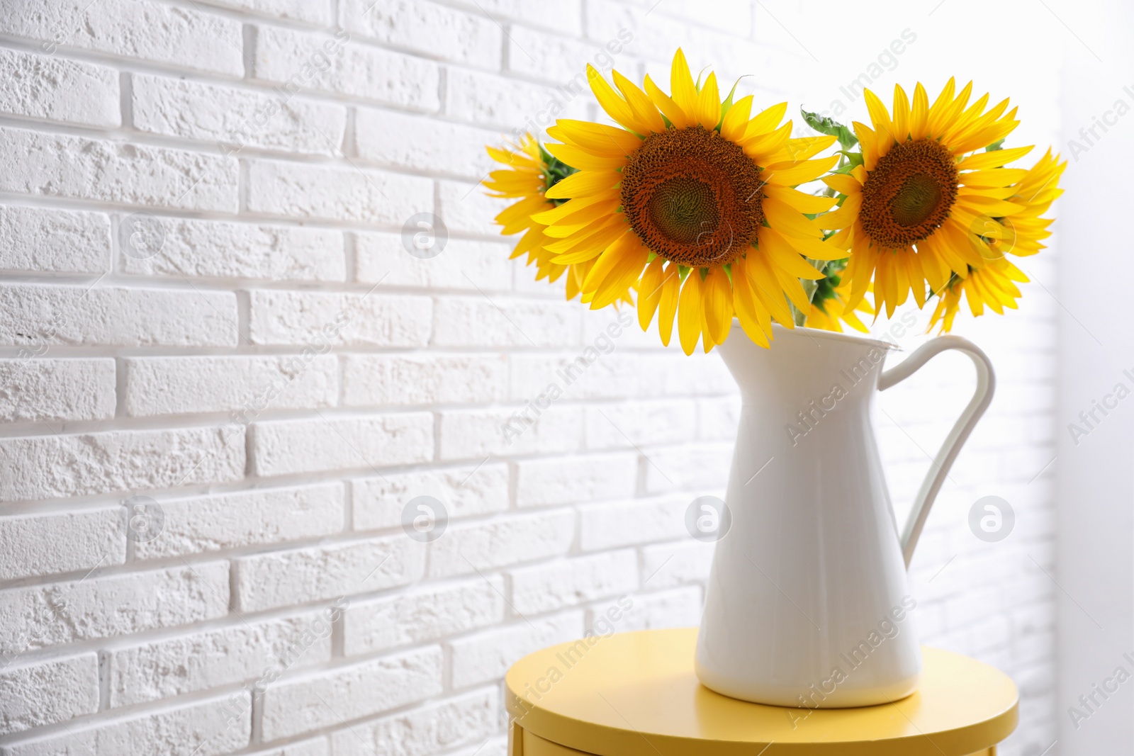 Photo of Bouquet of beautiful sunflowers on table near white brick wall. Space for text
