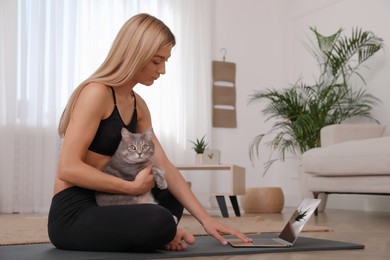 Photo of Beautiful woman with her cat watching online yoga class at home