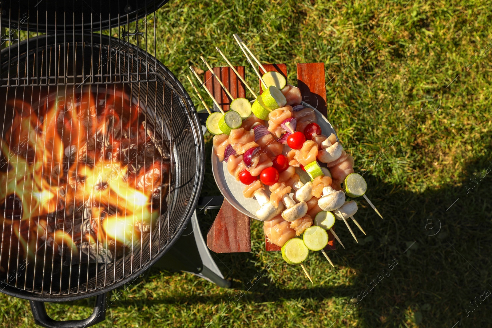 Photo of Skewers with meat and vegetables near barbecue grill outdoors, top view