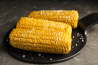 Photo of Delicious boiled corn with butter and salt on grey table, closeup