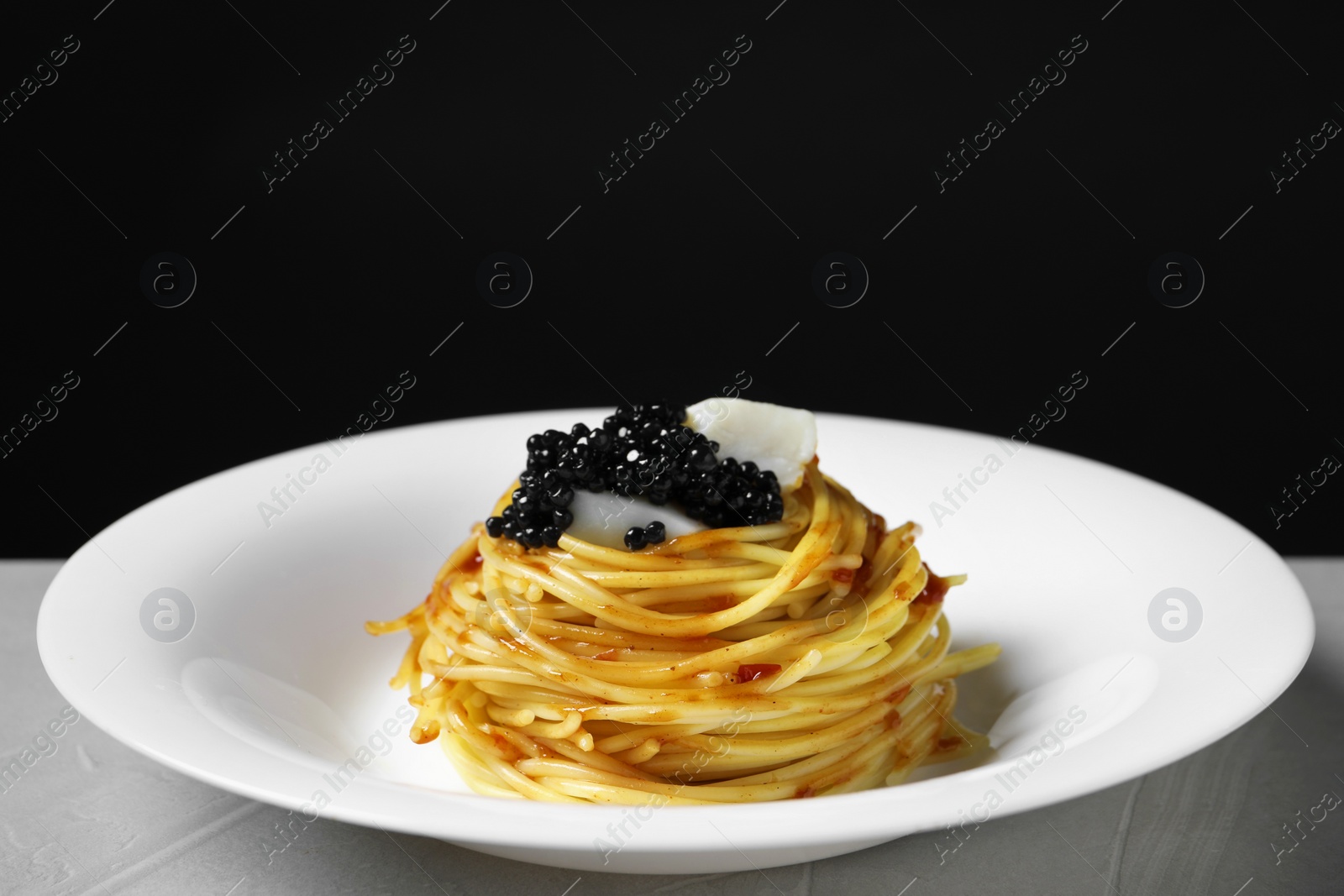 Photo of Tasty spaghetti with tomato sauce and black caviar on light grey textured table, closeup. Exquisite presentation of pasta dish