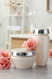 Hair care cosmetic products and beautiful flowers on light grey table in bathroom