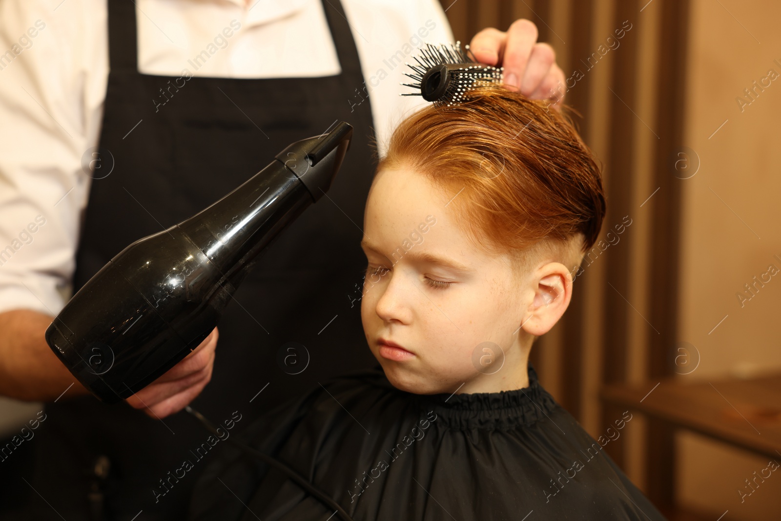 Photo of Professional hairdresser drying boy's hair in beauty salon, closeup