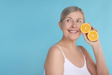 Photo of Beautiful woman with halves of orange rich in vitamin C on light blue background, space for text