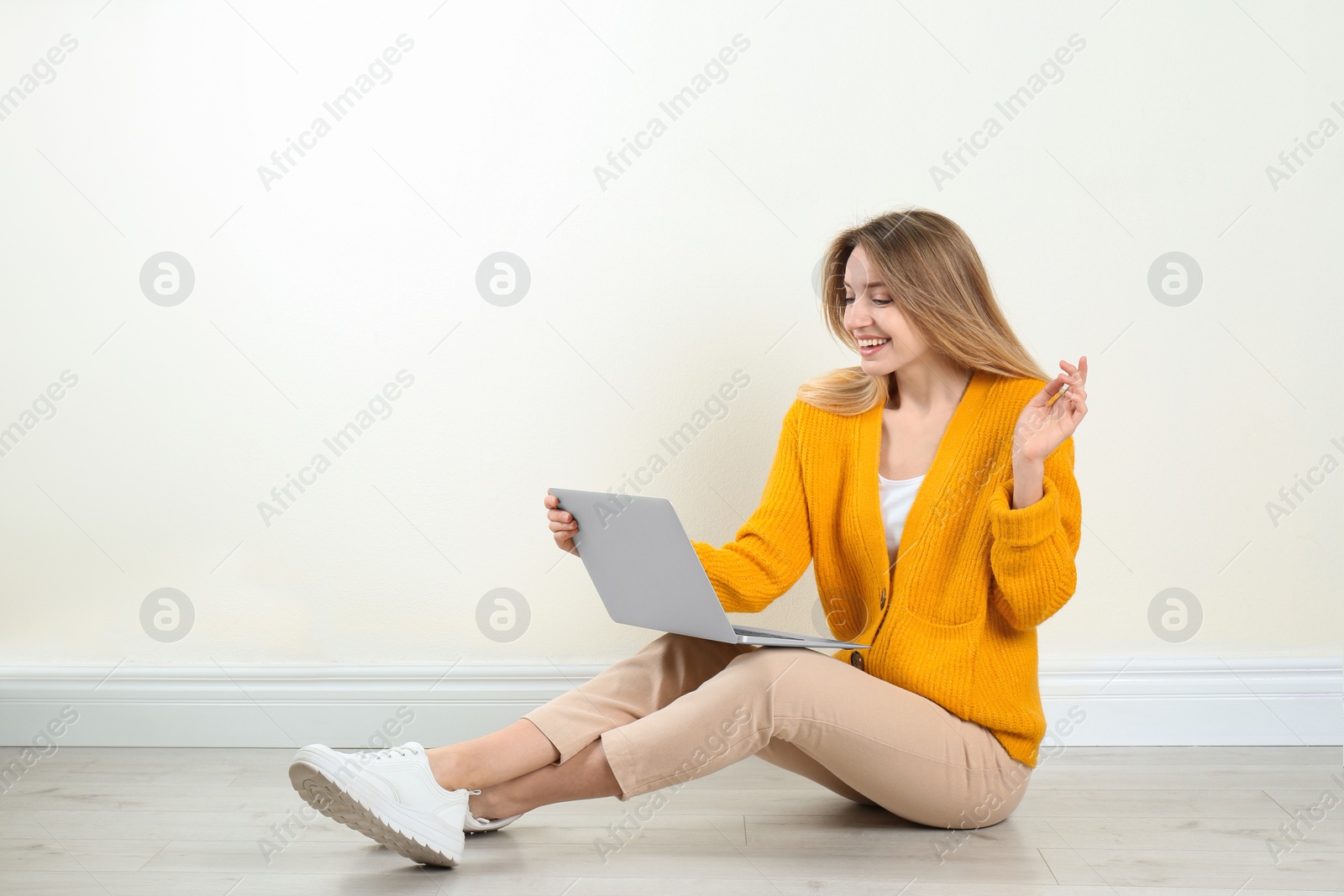 Photo of Young woman with laptop sitting on floor near light wall indoors. Space for text