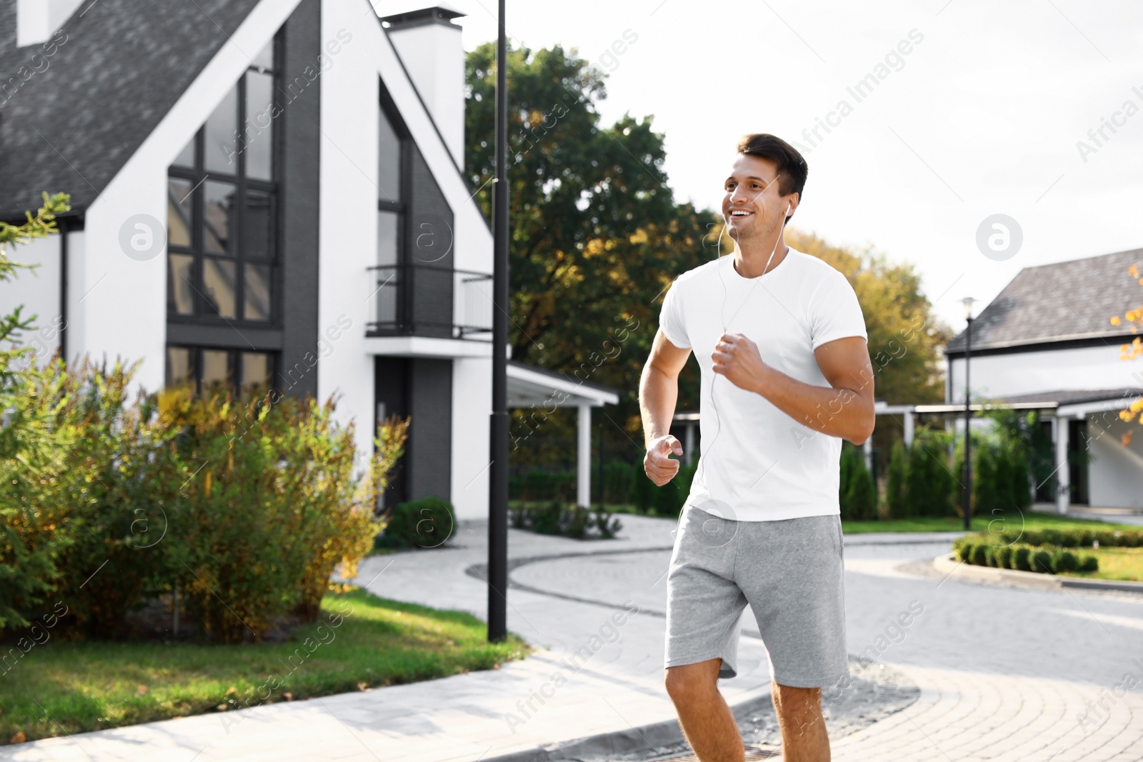 Photo of Young man with earphones running outdoors on sunny morning. Healthy lifestyle