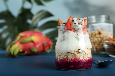 Glass jar of granola with pitahaya, yogurt and strawberries on blue wooden table, space for text