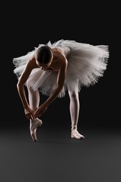 Photo of Young ballerina practicing dance moves on black background