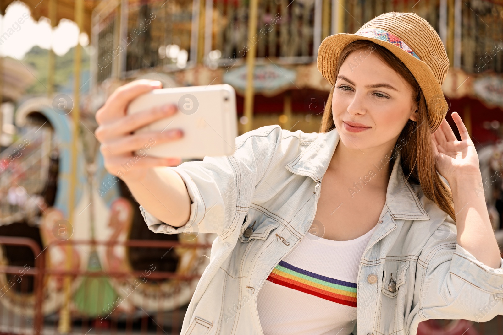 Photo of Young pretty woman taking selfie near carousel in amusement park