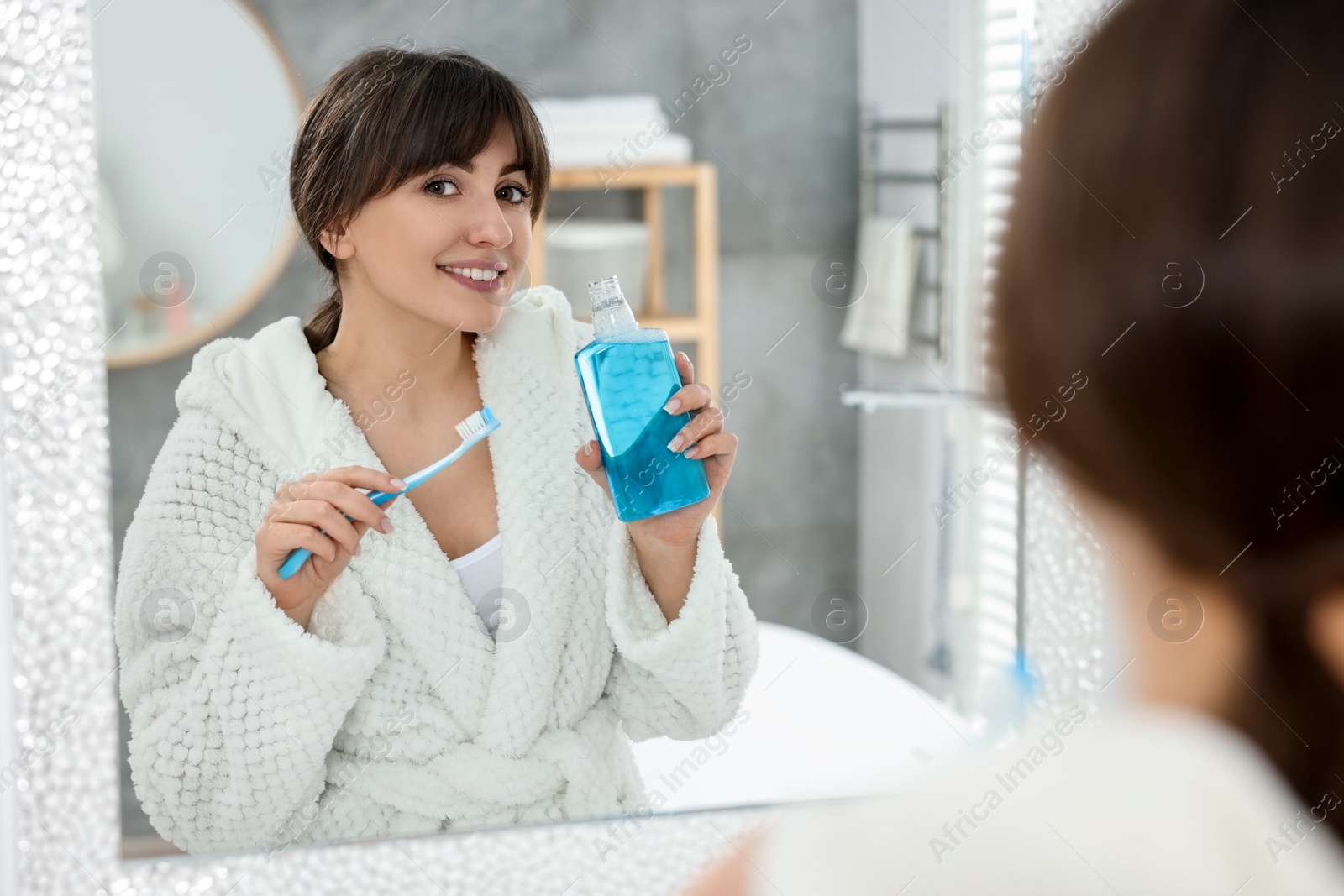 Photo of Young woman using mouthwash near mirror in bathroom