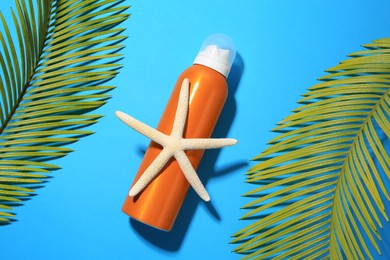 Photo of Sunscreen, starfish and tropical leaves on light blue background, flat lay. Sun protection care