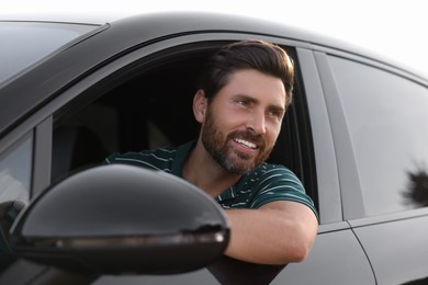 Photo of Enjoying trip. Happy bearded man driving his car, view from outside