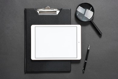 Modern tablet, clipboard, pen and magnifying glass on black background, flat lay. Space for text