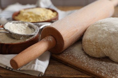 Photo of Rolling pin, flour and dough on wooden table, closeup