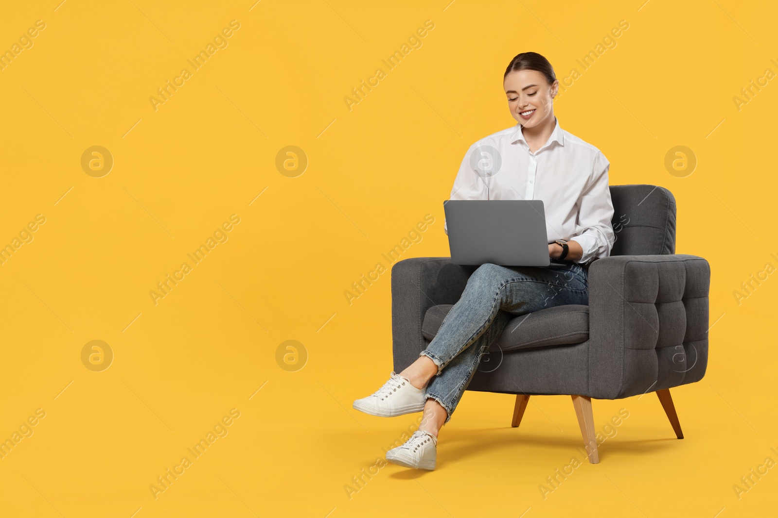 Photo of Happy woman with laptop sitting in armchair on orange background. Space for text