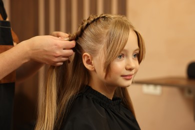 Photo of Professional hairdresser braiding girl's hair in beauty salon, closeup