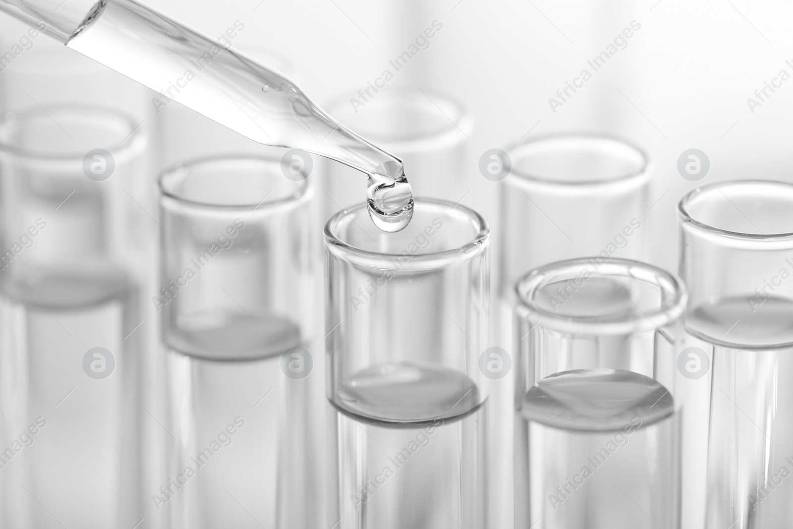 Photo of Laboratory analysis. Dripping liquid from pipette into glass test tube on blurred background, closeup