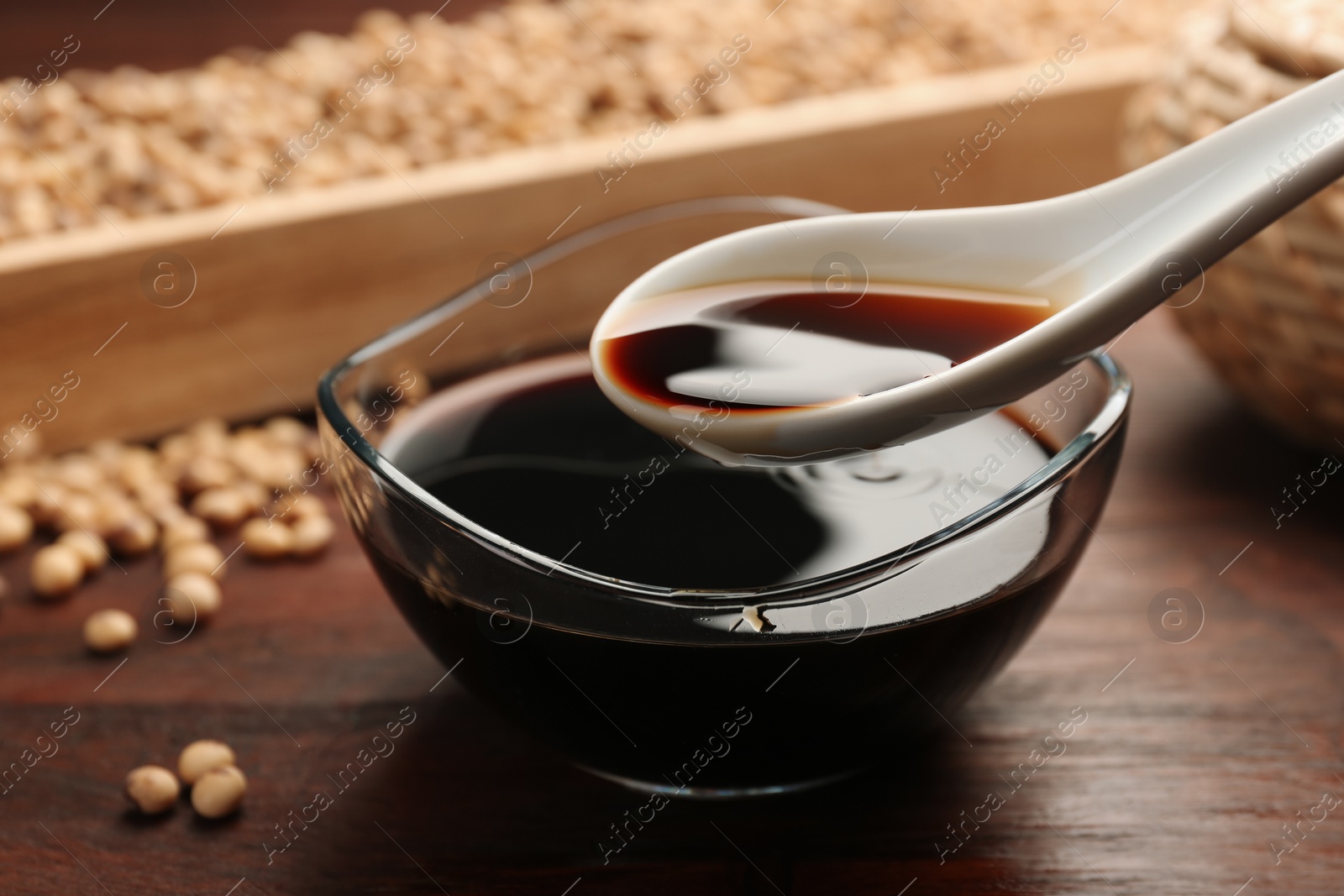 Photo of Taking soy sauce with spoon from bowl at wooden table, closeup