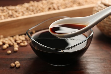 Taking soy sauce with spoon from bowl at wooden table, closeup