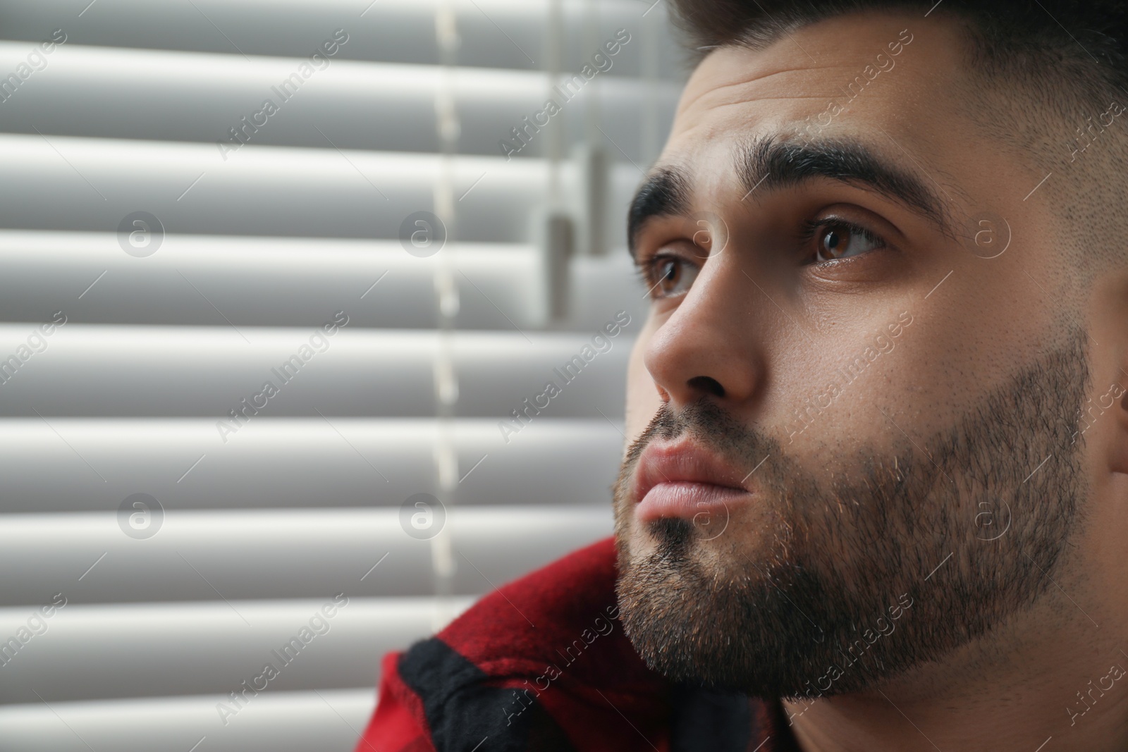 Photo of Sad young man near closed blinds at home. Space for text