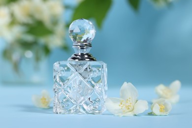 Photo of Aromatic perfume in bottle and beautiful jasmine flowers on light blue background, closeup