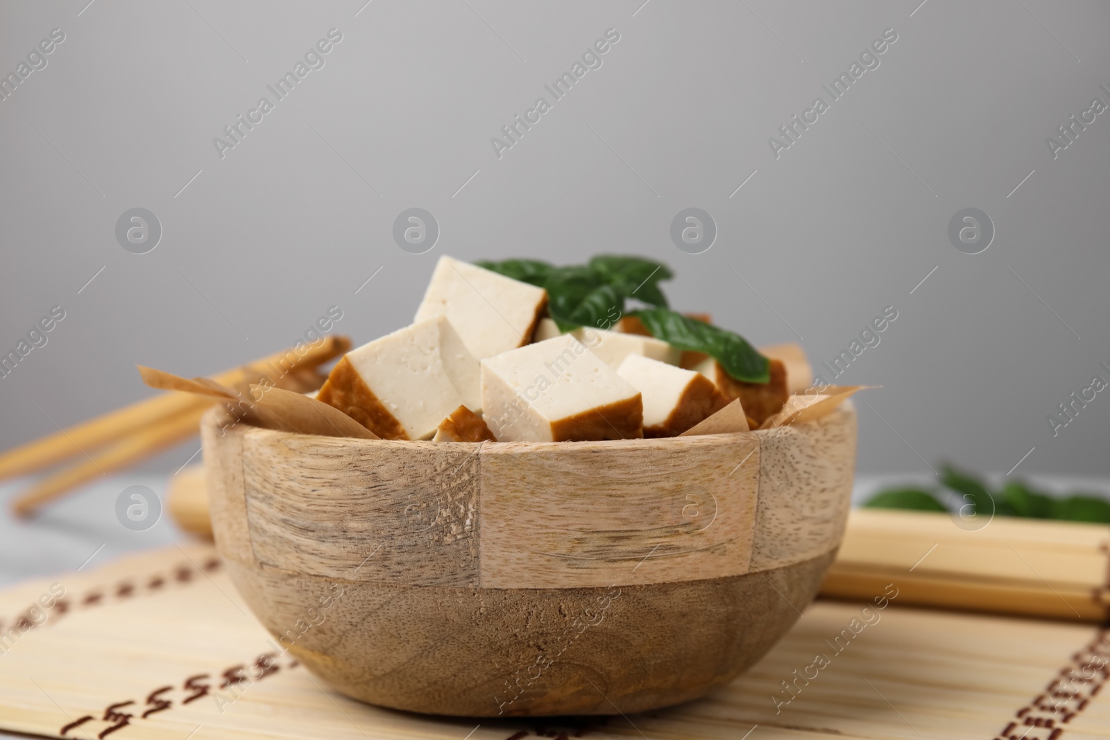 Photo of Bowl of smoked tofu cubes and basil on bamboo mat, closeup