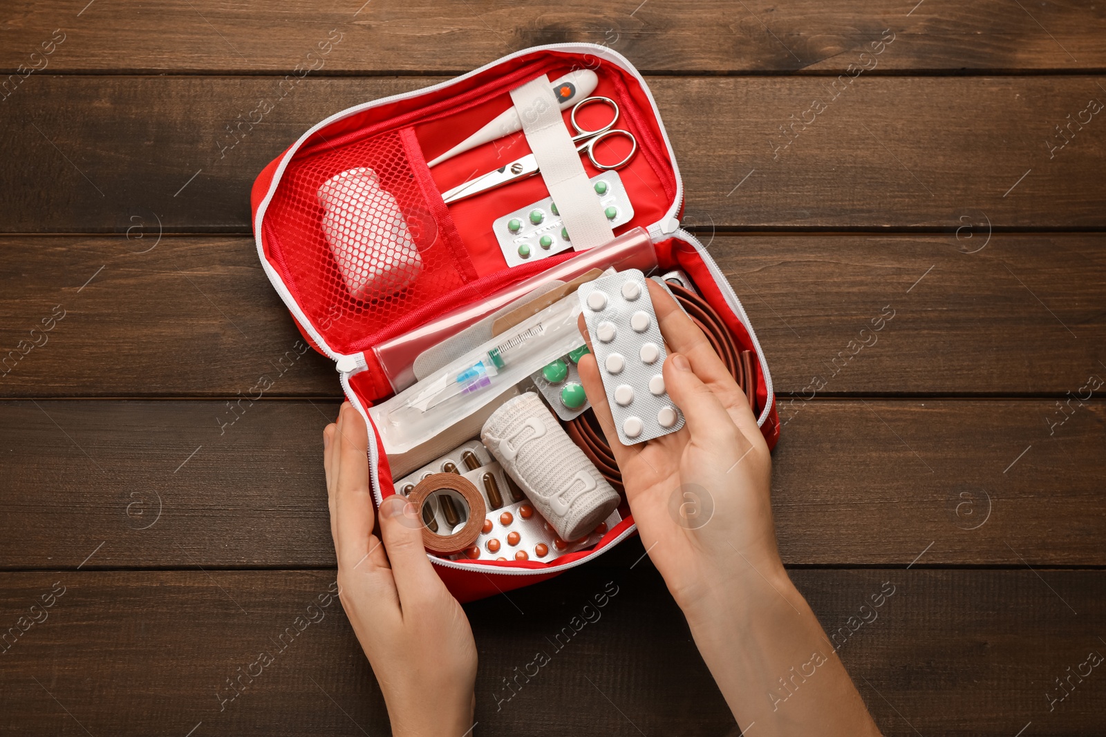 Photo of Woman taking pills from first aid kit at wooden table, top view