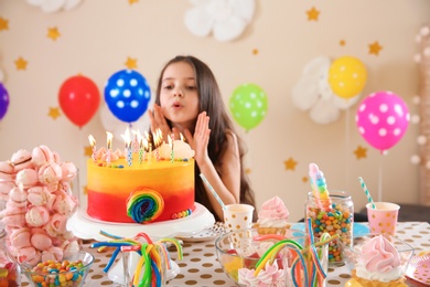 Photo of Cute little girl blowing out candles on her birthday cake indoors