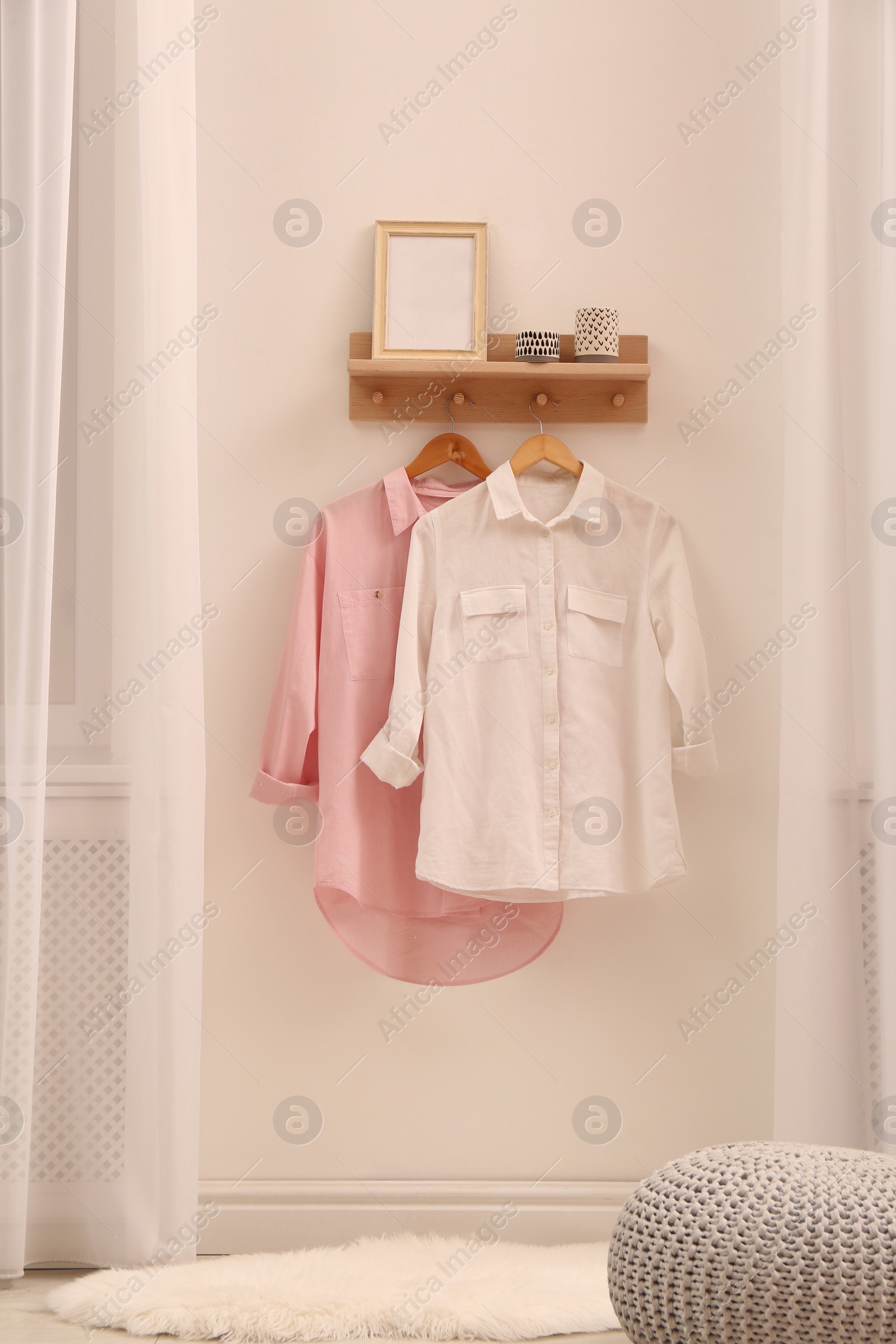 Photo of Wooden shelf with fashionable clothes and decorative elements on light wall in room. Interior design