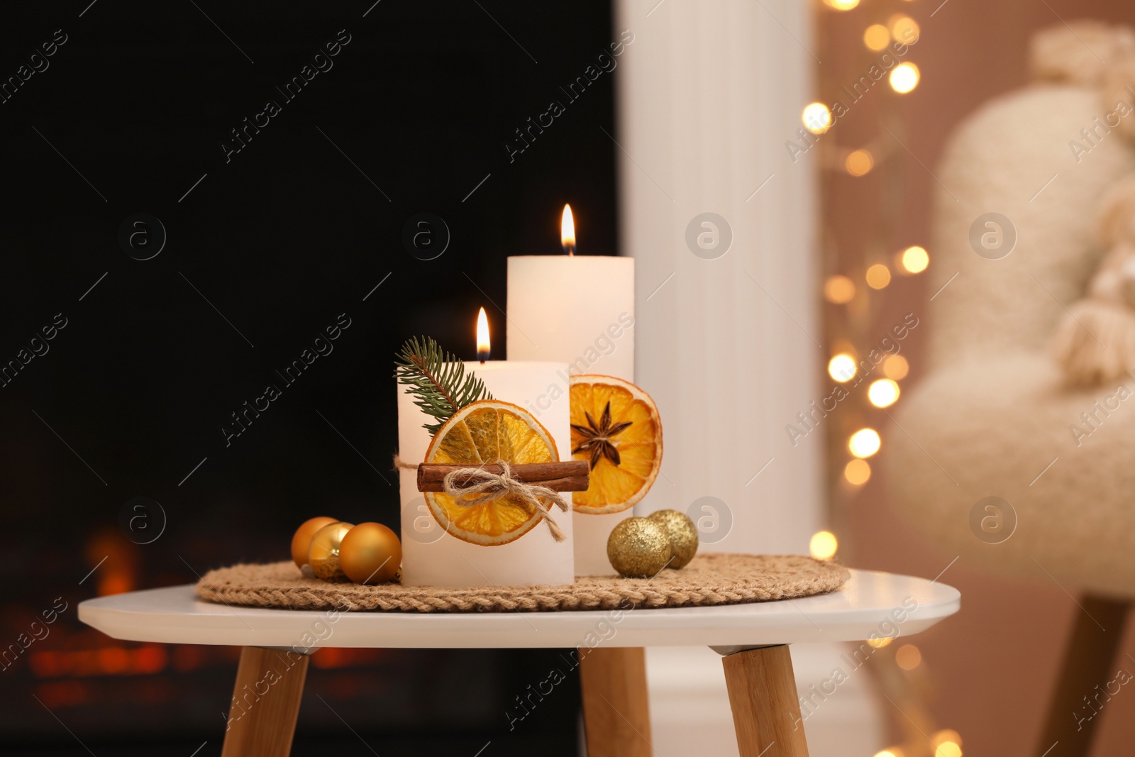 Photo of Beautiful burning candles decorated with dry orange slices and cinnamon sticks on white table indoors. Christmas atmosphere