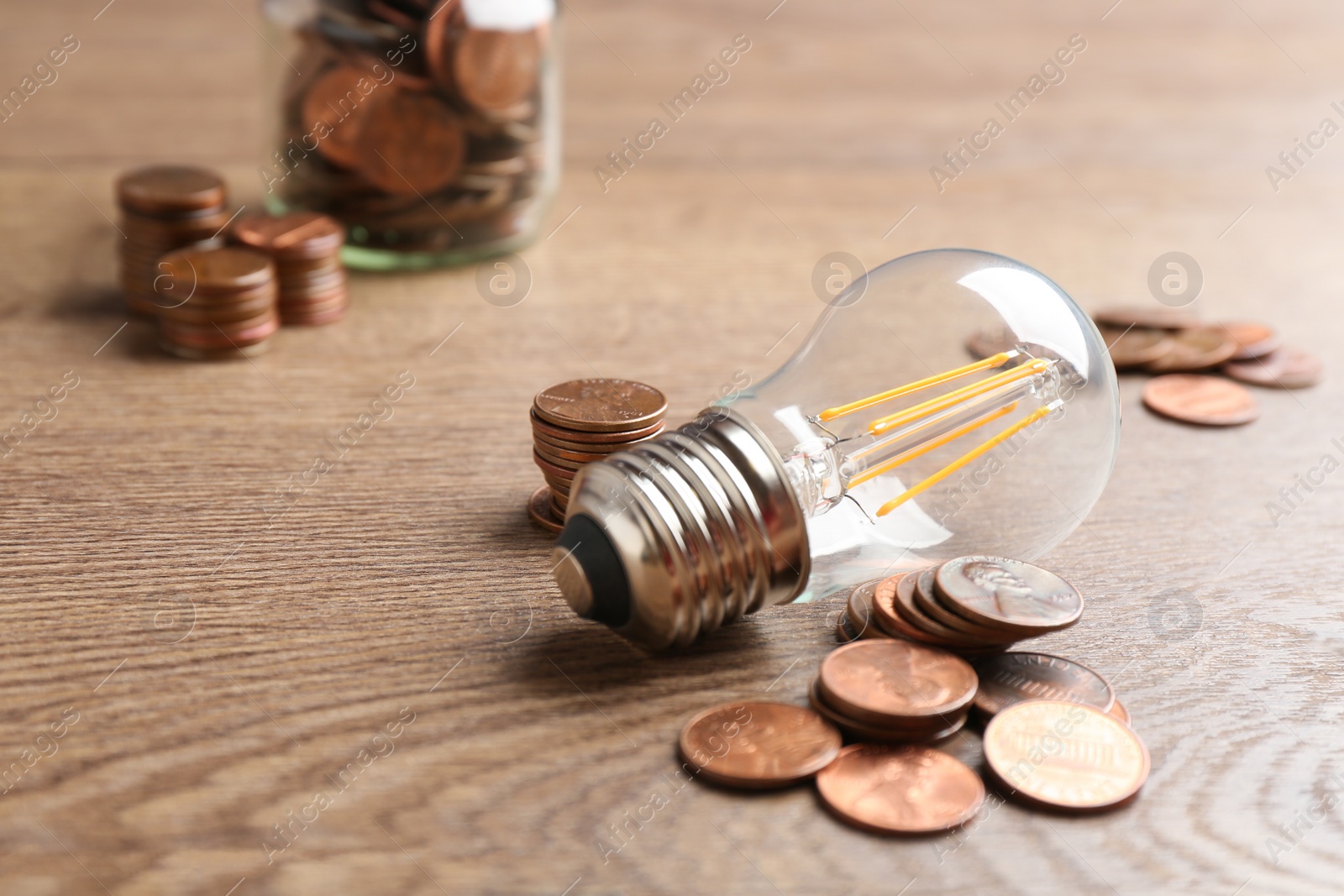 Photo of Lamp bulb and coins on wooden table, space for text. Money saving concept