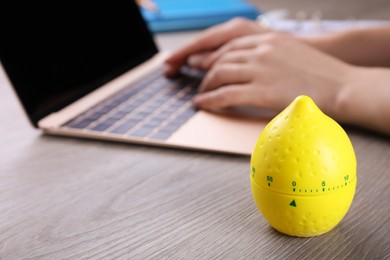 Woman working on laptop at wooden table, focus on kitchen timer in shape of lemon. Space for text