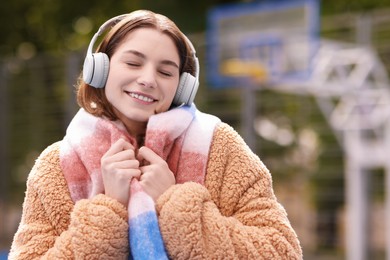 Photo of Beautiful woman in warm scarf listening to music outdoors