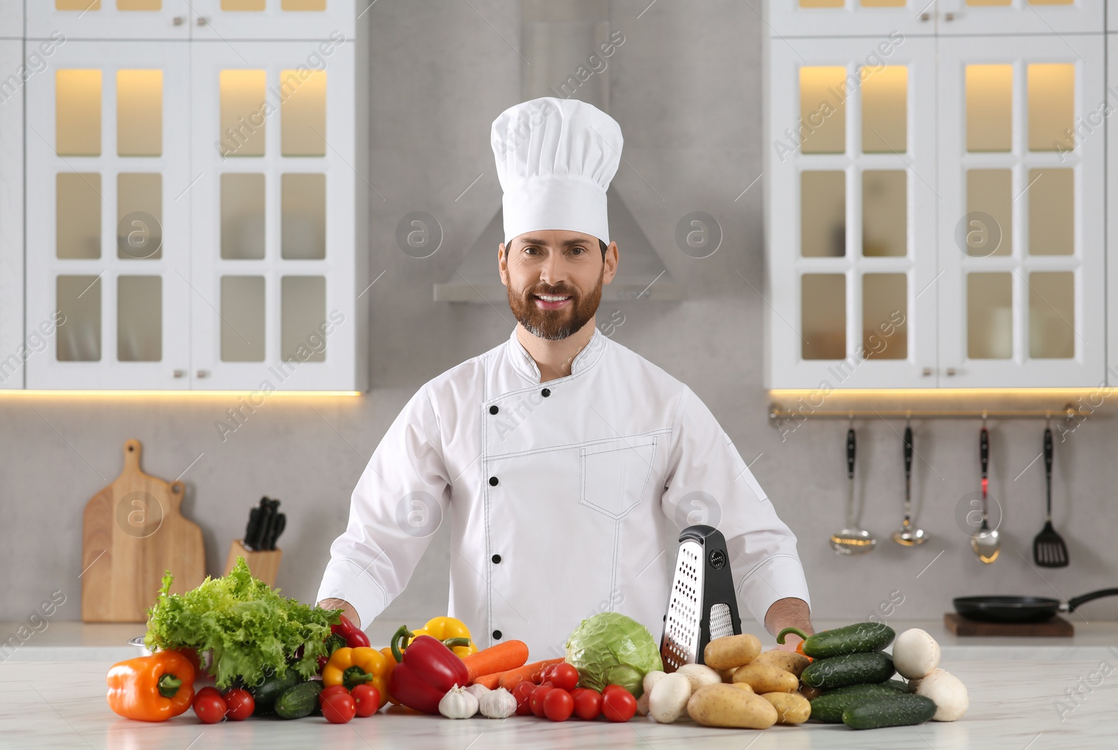 Photo of Portrait of happy professional chef near vegetables at marble table in kitchen